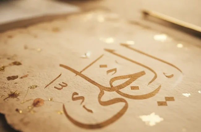 Close-up of gold Arabic calligraphy spelling 'Allah' on a reflective surface.