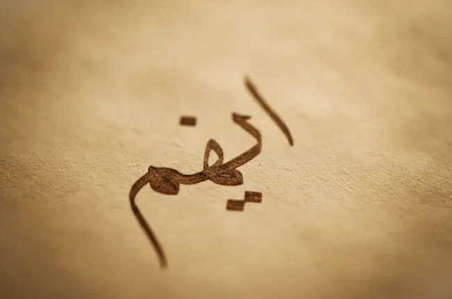 Close-up of brown Arabic calligraphy on parchment-like paper, an abstract decorative text.