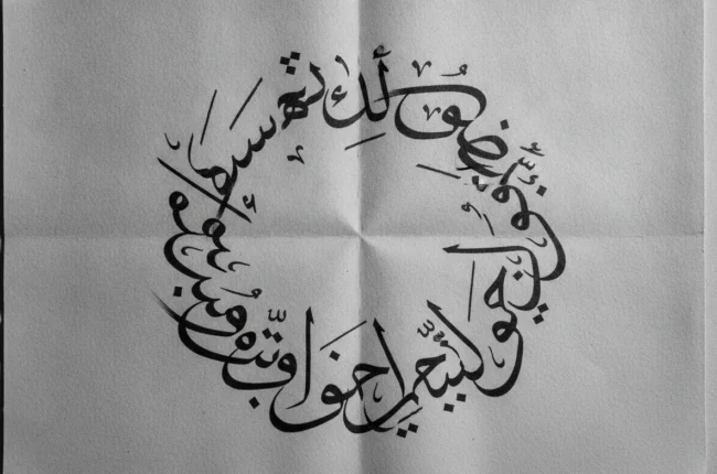 Decorative circular Arabic calligraphy on white paper forming a round design.