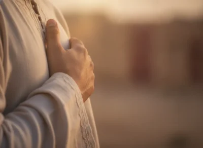 Close-up of a person placing a hand over their chest in a warm, sunlit setting.