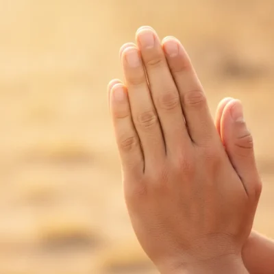 Hands pressed together in prayer against a warm, sunlit background.