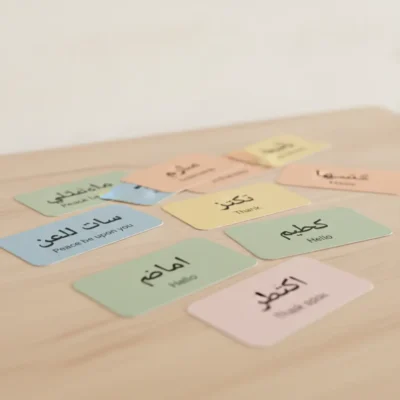 Set of small pastel language cards laid out on a table, showing Arabic phrases with English translations like Hello, Thank you, and Peace be upon you (greeting cards). تعلم العربية وحدك