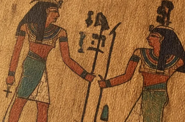 Ancient Egyptian relief of two standing figures in profile facing each other, one with a red crown and the other with a blue headdress, exchanging a vertical staff amid hieroglyphs.