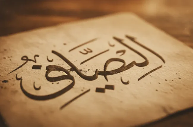 Close-up of elegant Arabic calligraphy on a brown parchment, likely spelling the word 'Allah'.